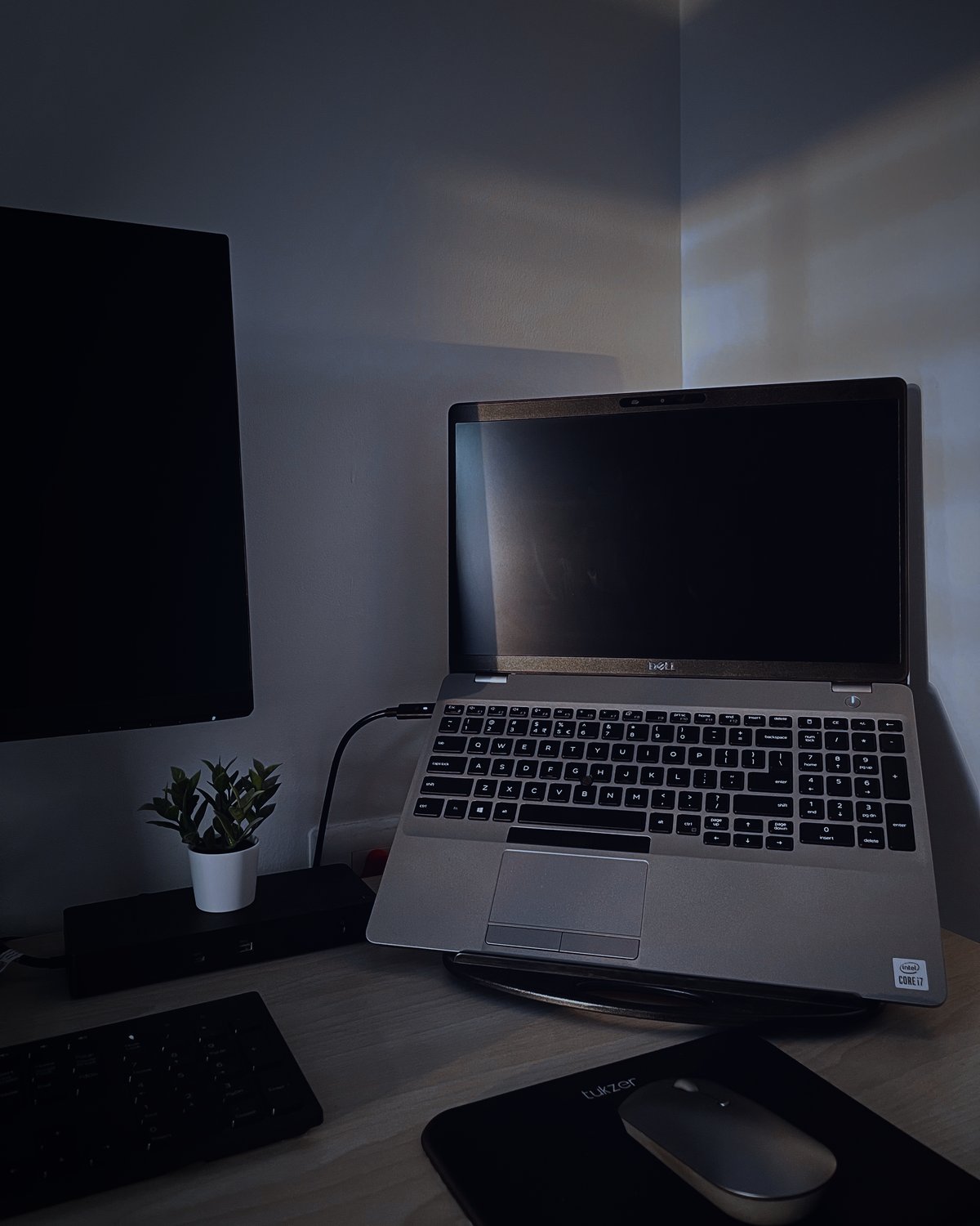 Służbowy laptop na podstawce przy biurku, obok monitor i stacja dokująca